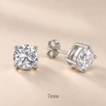 Pair of 7mm round CZ four-claw sterling silver stud earrings with open baskets, posts and butterfly backs on beige, visibly labelled 7mm.