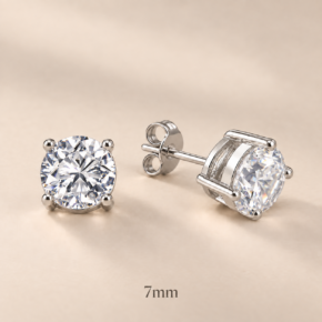 Pair of 7mm round CZ four-claw sterling silver stud earrings with open baskets, posts and butterfly backs on beige, visibly labelled 7mm.