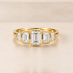 Front view of five graduated emerald-cut lab-grown diamonds in yellow-gold rub-over settings