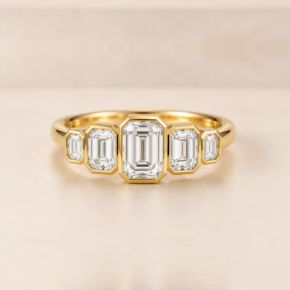 Front view of five graduated emerald-cut lab-grown diamonds in yellow-gold rub-over settings